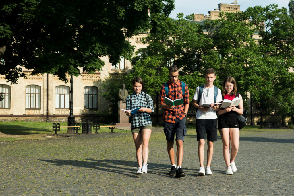 Estudantes caminhando em campus de universidade carregando seus livros; veja o que são os Summer programs e como funcionam os cursos de verão para estudantes