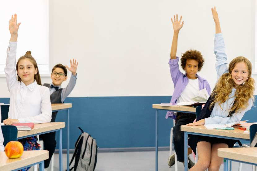 estudantes felizes de mãos levantadas em sala de aula para o dia do estudante