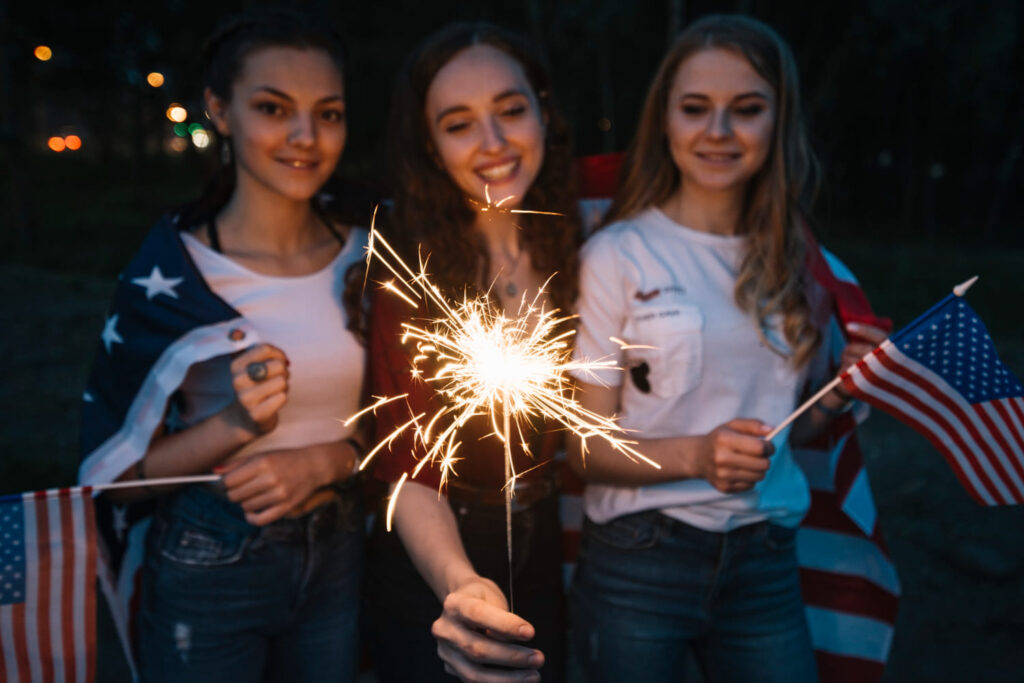 Jovens norte-americanos segurando bandeiras dos Estados Unidos durante o dia da independência; entenda se 4 de julho é feriado no Brasil ou só nos EUA