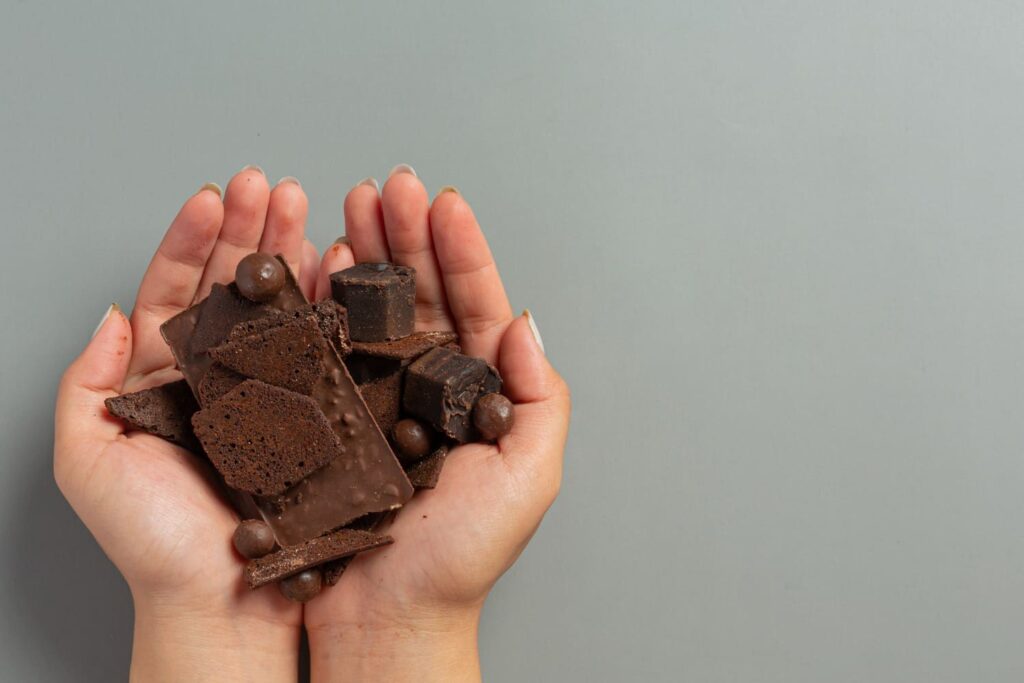 Mão segurando pedações de barra de chocolate; saiba porque o Dia Mundial do Chocolate é comemorado em 7 de julho e veja frases para celebrar
