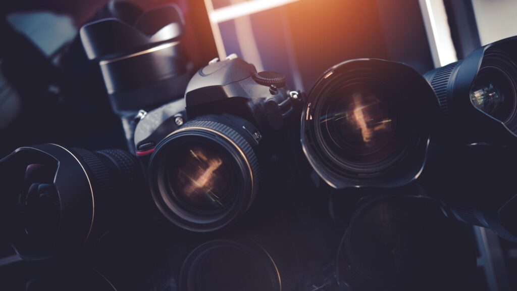 Máquinas e equipamentos fotográficos posicionados lado a lado. A imagem representa o uso da Fotografia e quais são os componentes necessários para o registro, como: lentes e câmeras.