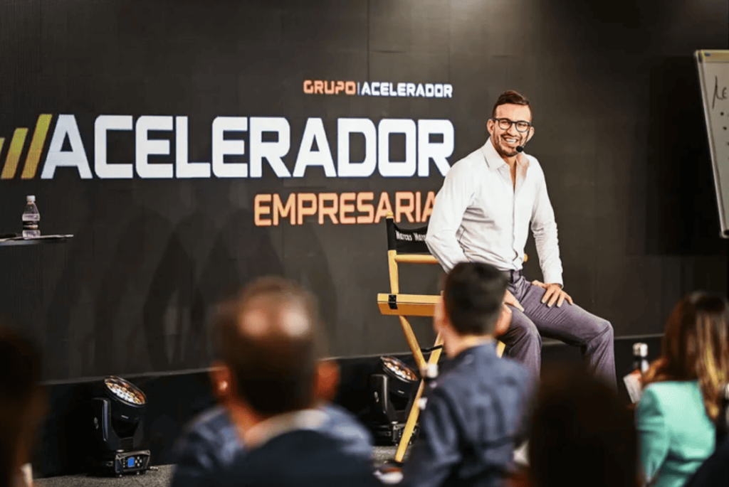 Marcus Marques palestrando em frente a um banner de seu programa 