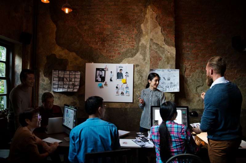 Equipe de profissionais discutindo projetos criativos em um ambiente de trabalho, com computadores e imagens visuais, ilustrando o que faz um designer gráfico.
