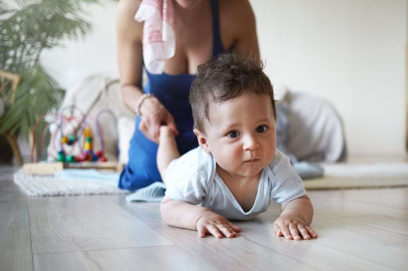 Bebê engatinhando com o apoio de um adulto, destacando a importância da fisioterapia respiratória nos bebês para o desenvolvimento motor e respiratório.