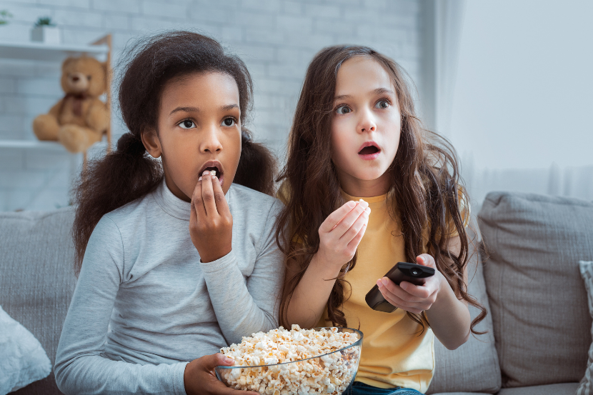 crianças com expressão de susto e curiosidade comendo pipoca e assistindo stranger things