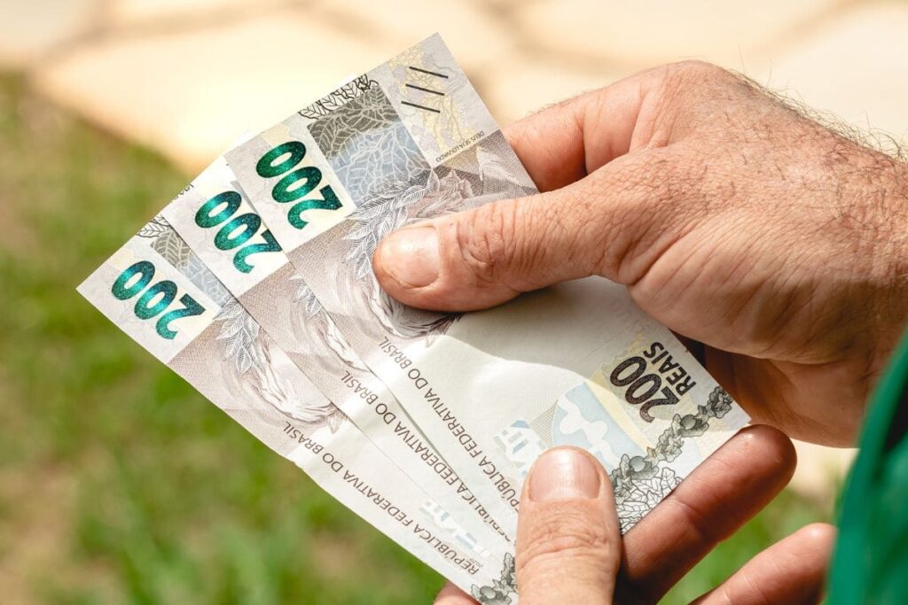 Homem segurando notas de 200 reais na mão; veja quem tem direito ao pagamento do décimo terceiro salário