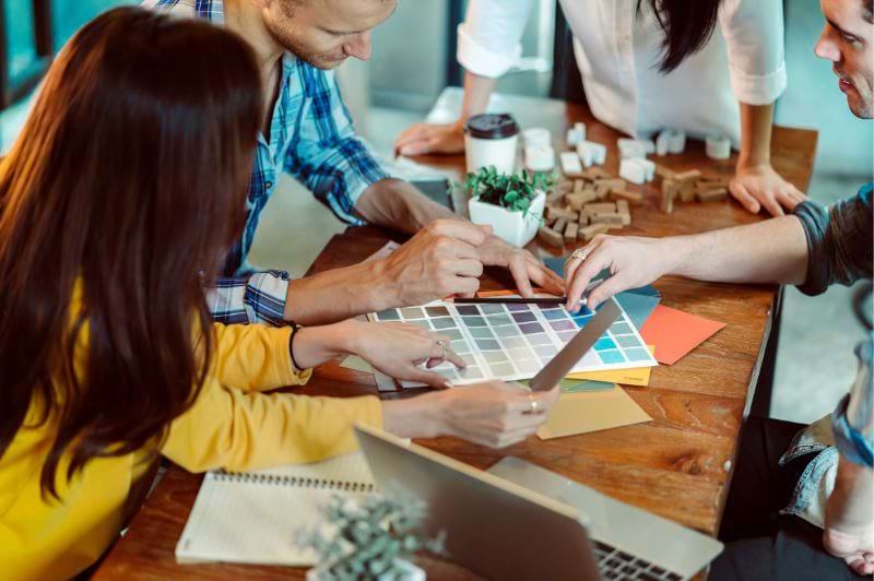 Profissionais das áreas do design gráfico discutindo paletas de cores e materiais em um ambiente criativo.