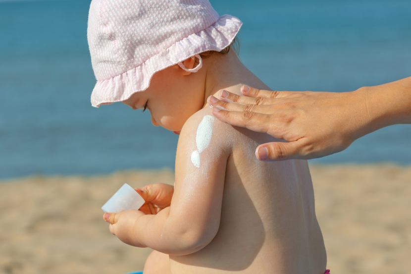 mãe passando protetor solar em bebê na praia para cuidados com crianças no verão