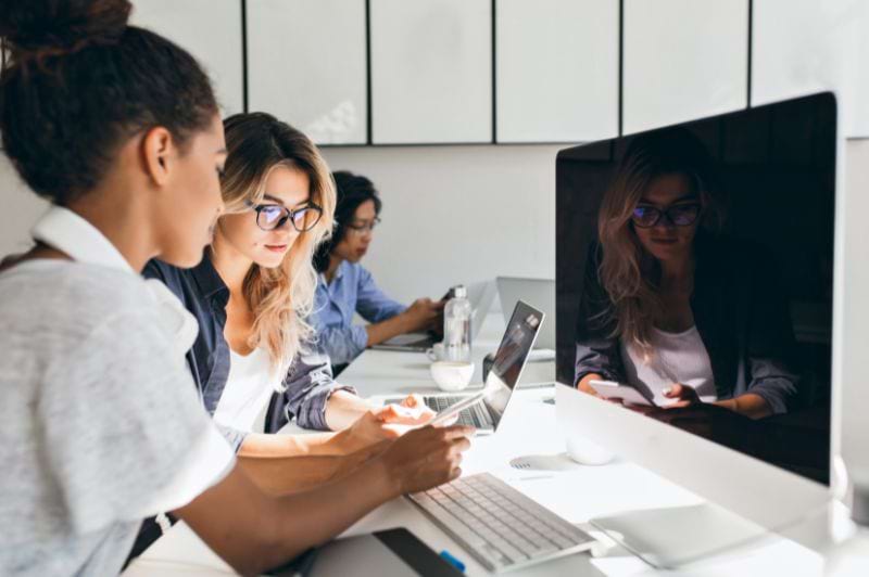 Grupo de estudantes em um ambiente de trabalho moderno, focados em seus laptops durante um curso de pós-graduação em Análise e Desenvolvimento de Sistemas.
