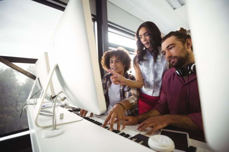 Desenvolvedores de sistemas colaborando em um ambiente de trabalho moderno, aprimorando suas habilidades e discutindo soluções técnicas, com foco no crescimento na área de TI.
