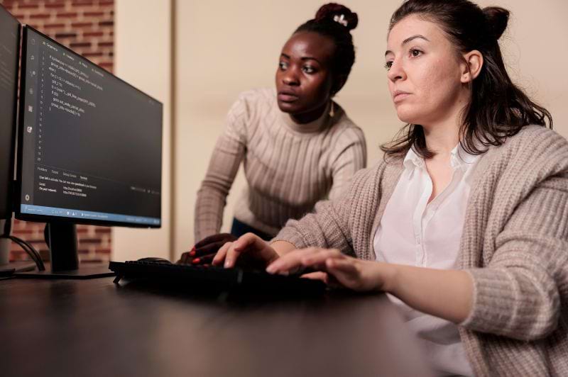 Desenvolvedores de sistemas colaborando em um ambiente de trabalho moderno, aprimorando suas habilidades e discutindo soluções técnicas, com foco no crescimento na área de TI.