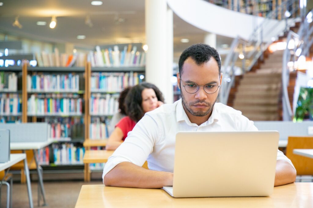 Estudante em biblioteca usando notebook, representando a pedagogia EAD e o curso de Pedagogia a distância reconhecido pelo MEC.