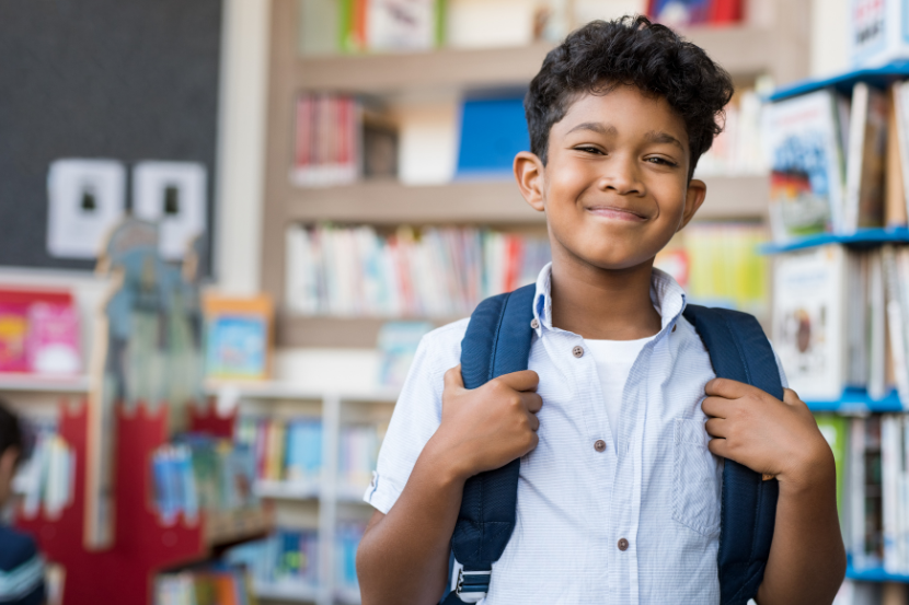aluno feliz na escola com mochila nas costas e biblioteca ao fundo
