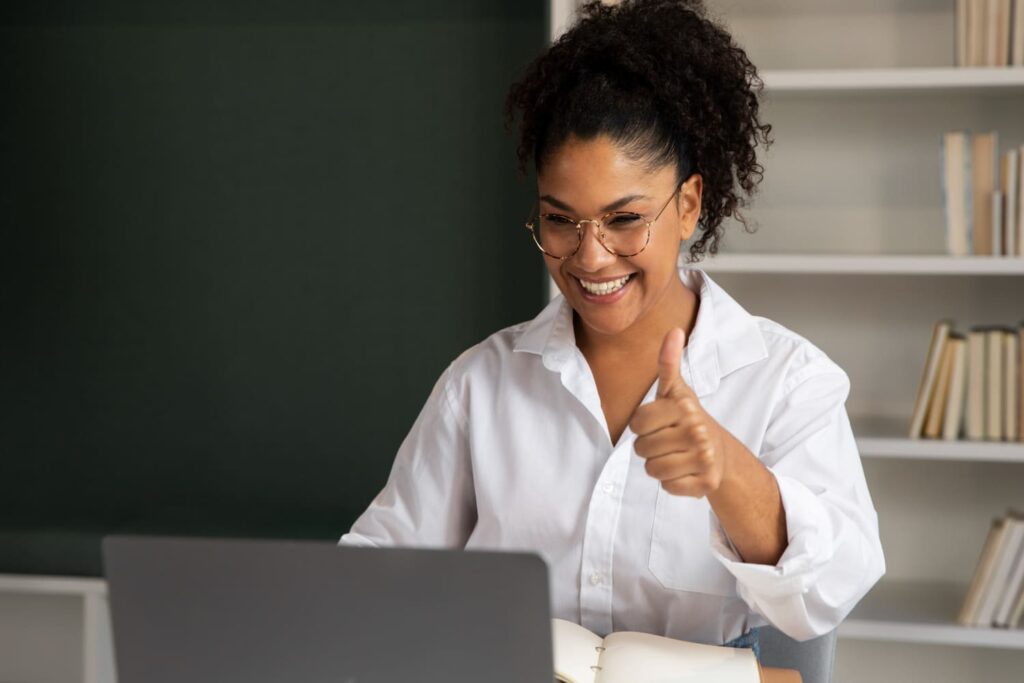 Professora feliz dando aula online pelo computador; confira as pós-graduações em educação com os melhores salários