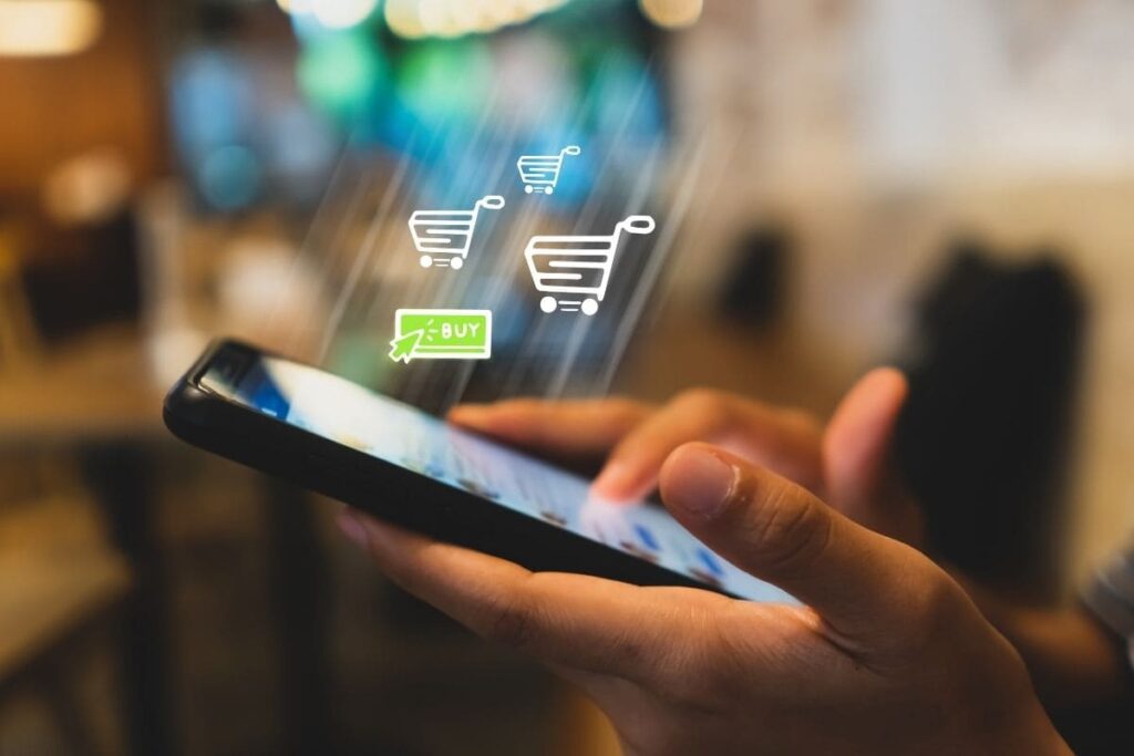 Mão de pessoa segurando celular mostrando que ela está fazendo compras online. Marketing Digital vale a pena para quem quer trabalhar com e-commerce?