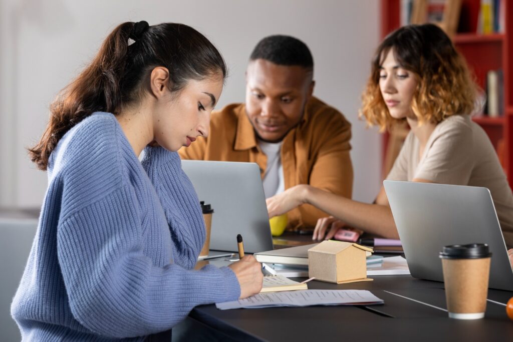 Estudantes de ciência da computação trabalhando juntos em projeto acadêmico com notebooks e anotações, preparando trabalho de conclusão de curso (TCC).