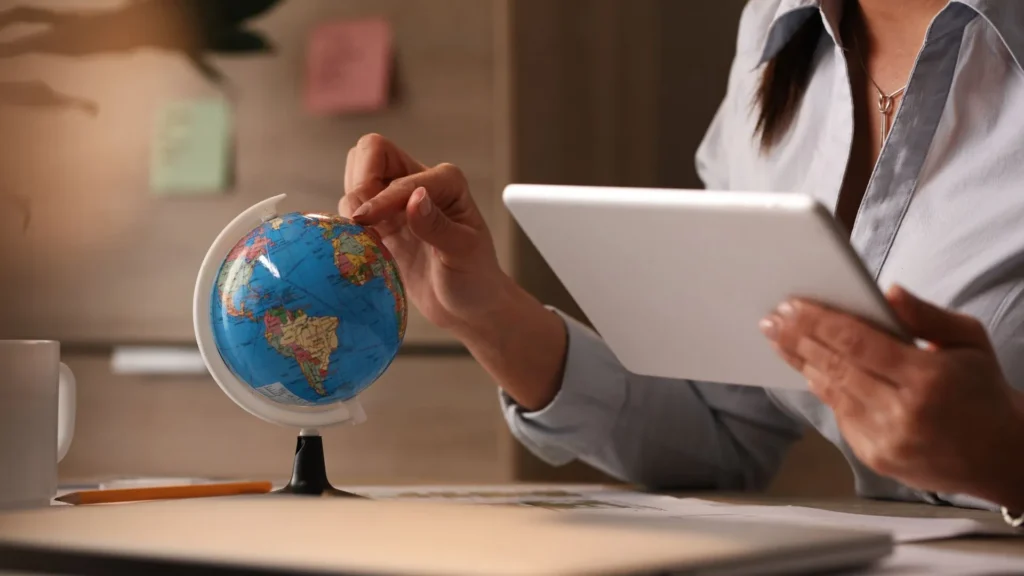 Profissional de marketing internacional, apontando o dedo no globo, enquanto usa um tablet para trabalhar.