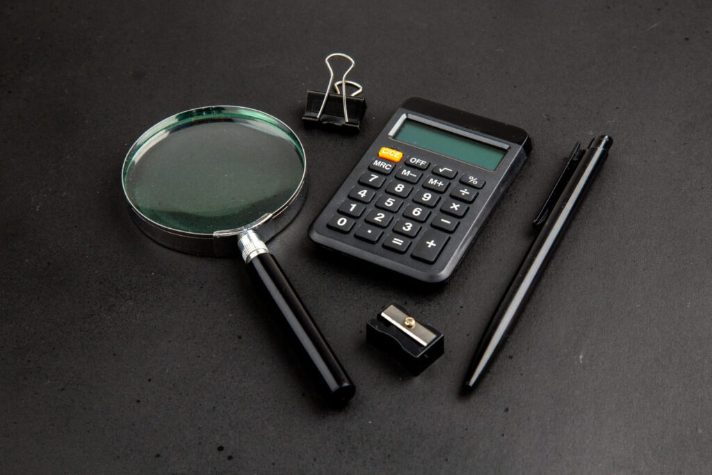 Vista inferior de uma lupa, calculadora, prendedor de papel, caneta e apontador; Contabilidade forense: veja o que faz o profissional especializado na área