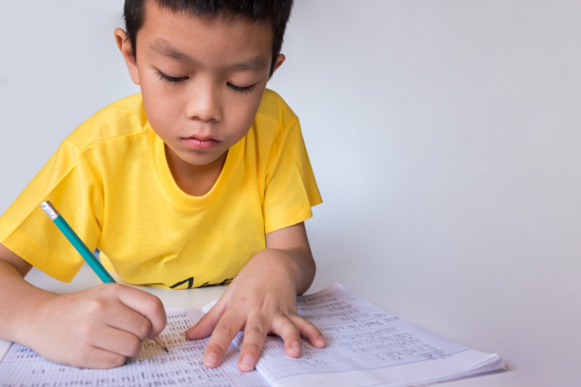 criança segurando lápis praticando atividades de caligrafia no caderno