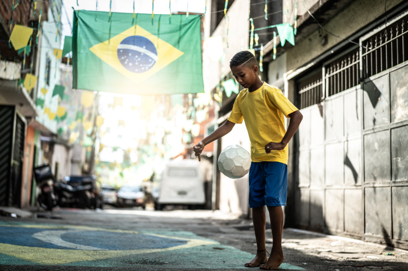 criança brincando de futebol em rua pintada com bandeira do Brasil 