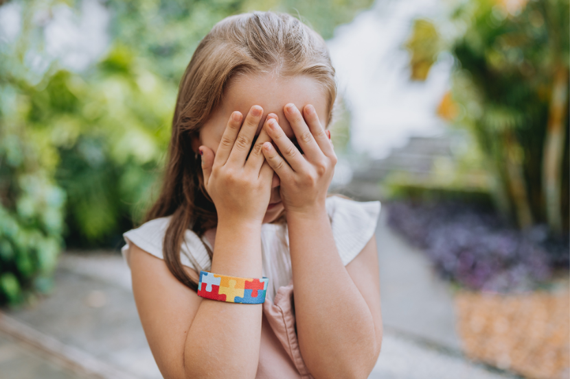 criança com pulseira de autismo tapando os olhos com as mãos