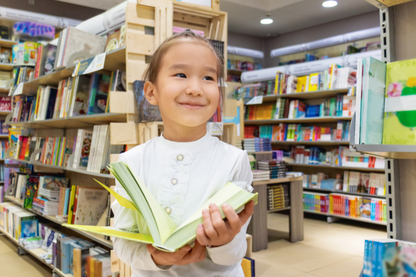 criança na biblioteca com livro na mão