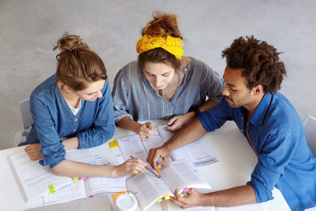 Alunos de graduação estudando as matérias da grade curricular do curso de Serviço Social. Foco na mesa com livros abertos e muitas anotações realizadas pelos estudantes.