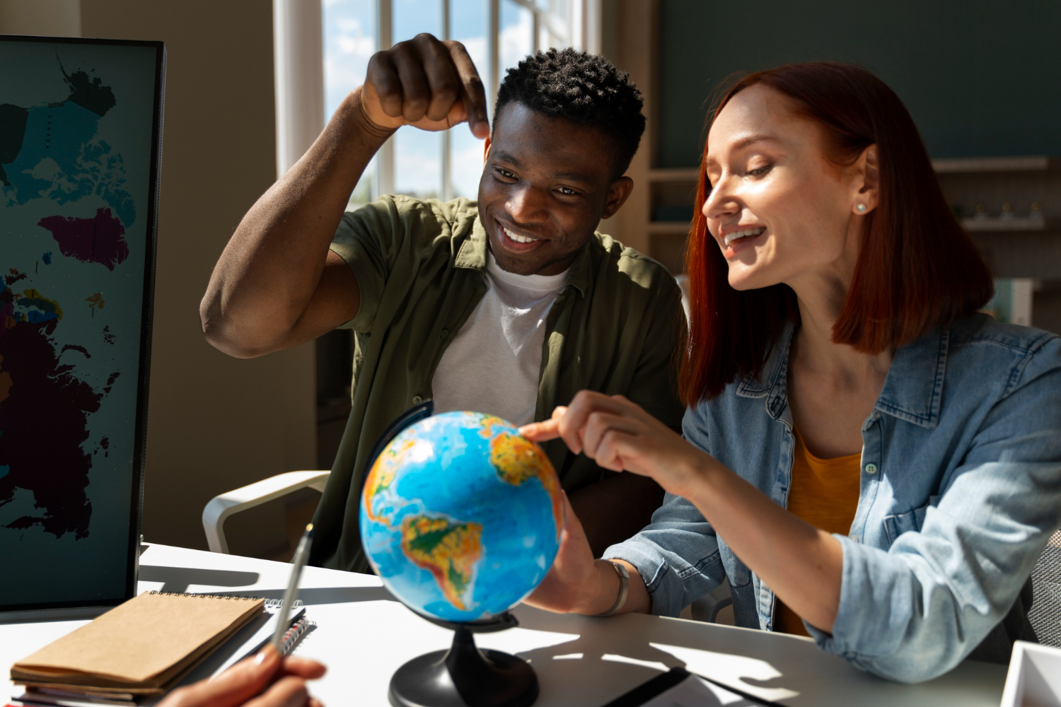 Homem e mulher olhando um globo, em cima de uma mesa, mostrando que curso de idiomas vale a pena.
