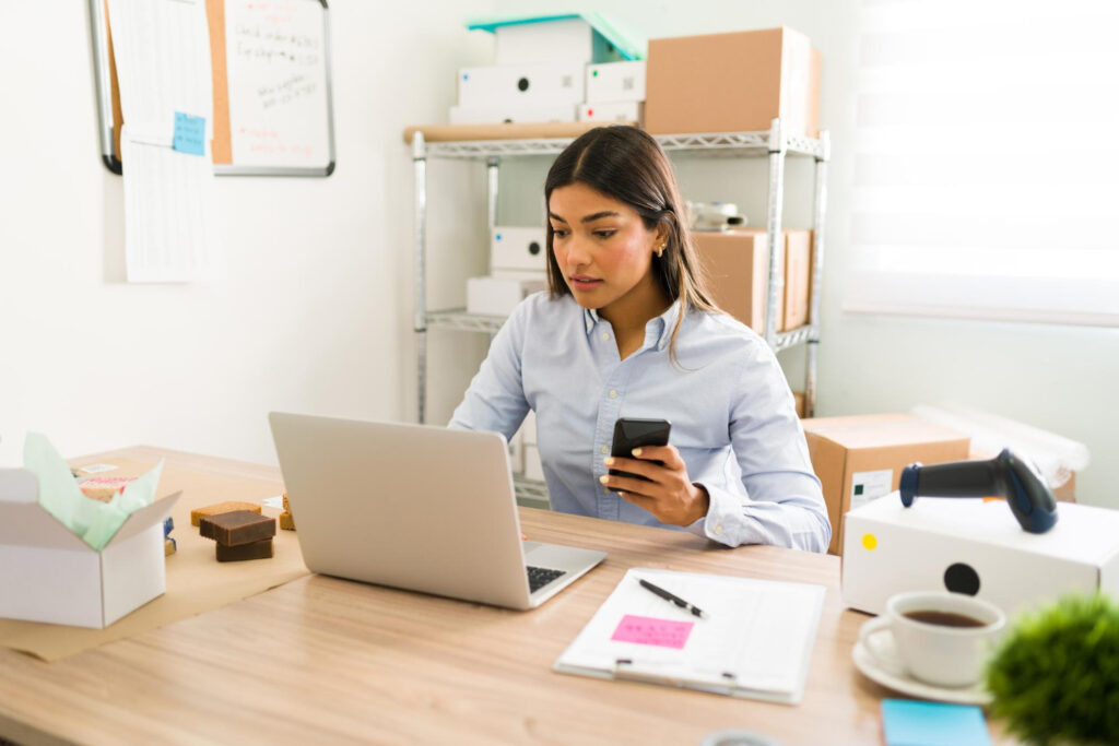 Estudante de Gestão Comercial usando notebook e celular, representando a escolha entre Gestão Comercial presencial ou EAD e diferentes modalidades de estudo.
