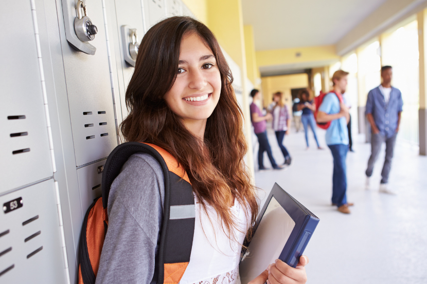 aluna do ensino médio sorridente na escola com material na mão e mochila