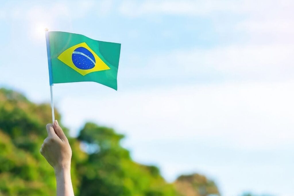 Mão de pessoa levantando bandeira do Brasil para o alto; Copa do Mundo e Enem: veja como o assunto pode ser usado para estudar