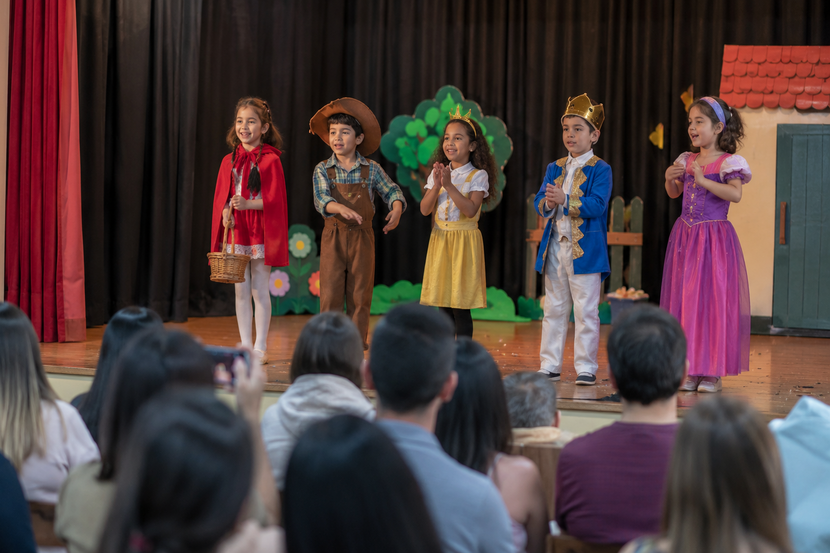 crianças apresentando peça de teatro infantil para pais em auditório escolar