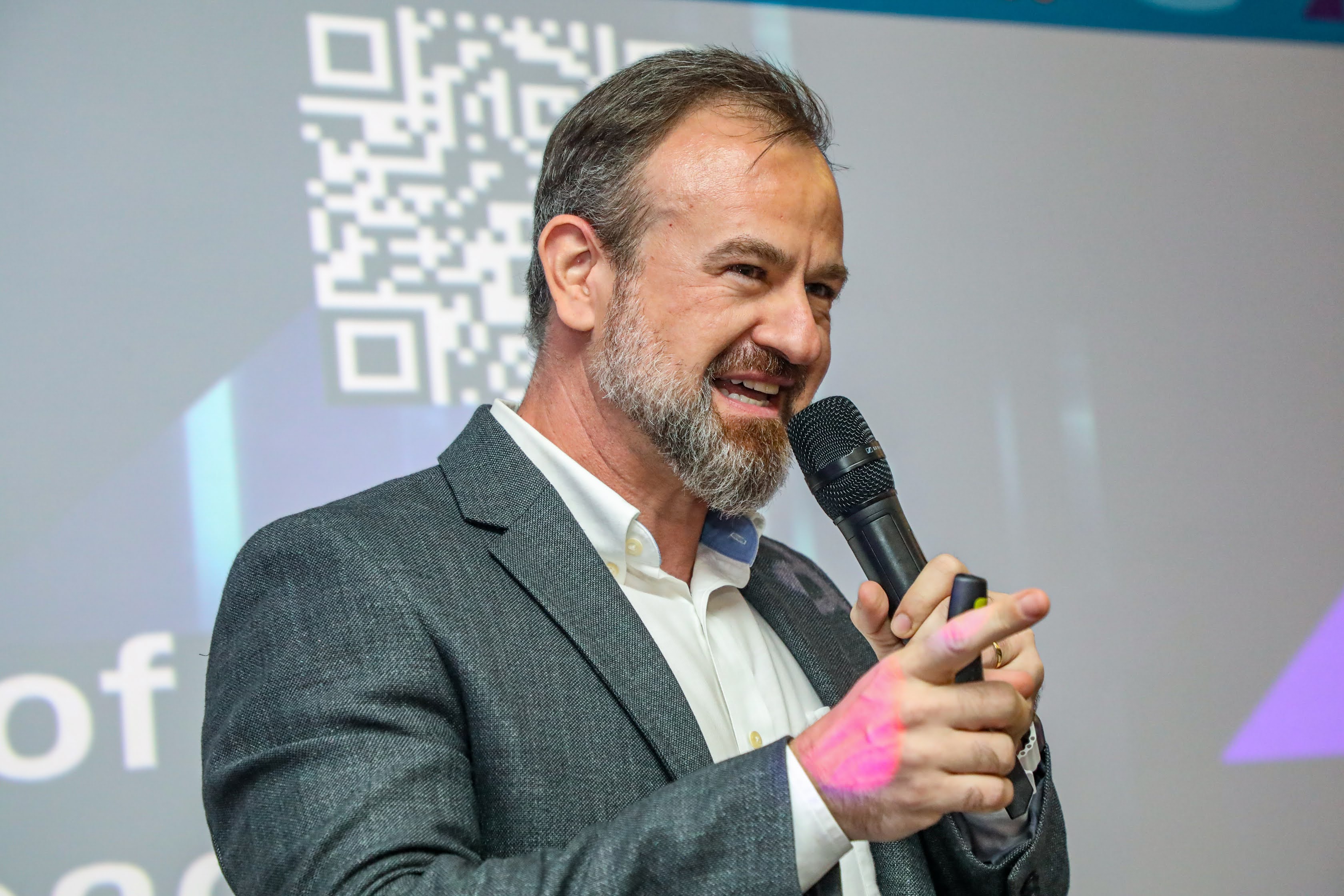 Mario Trentim em palco durante uma palestra, representando o conceito de maturidade de gestão, com público ao fundo e ambiente de conferência.