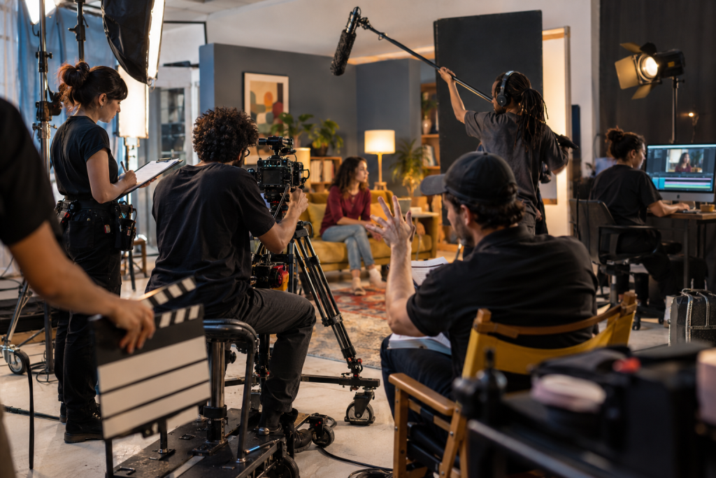 Equipe de profissionais de Cinema e Audiovisual trabalha em um set de filmagem com câmera, microfone e estação de edição.