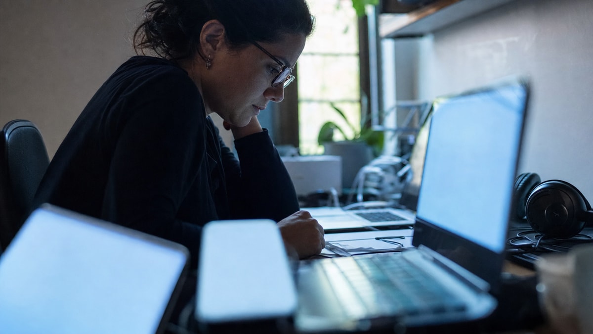 O custo da conexão constante Pessoa diante de vários dispositivos de trabalho, em uma cena que sugere interrupções e atenção fragmentada.
