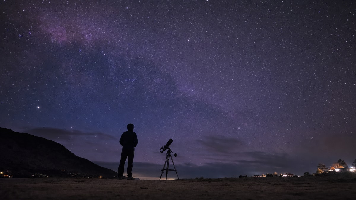 Pessoa observa o céu estrelado com um telescópio para compreender o universo