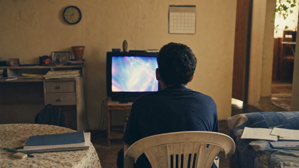 Adolescente acompanha uma programação televisiva em uma sala doméstica dos anos 2000