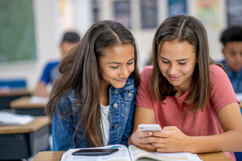duas meninas mexendo no celular em sala de aula 