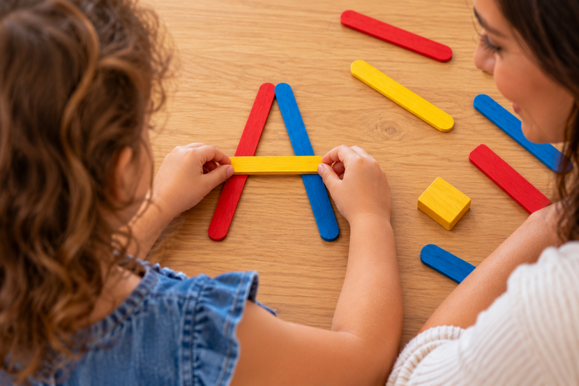 Criança fazendo atividade de vogais na Educação Infantil com palitos coloridos